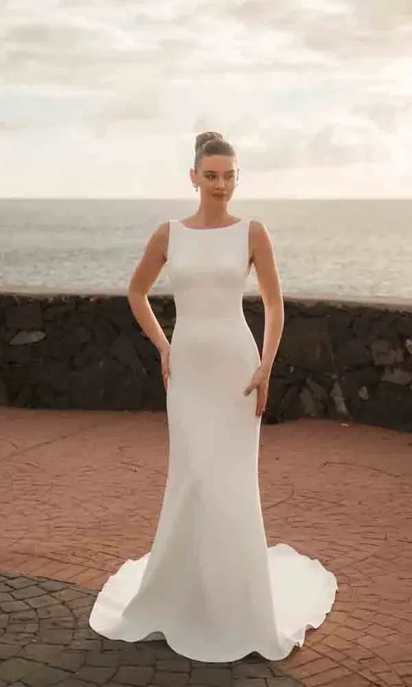 Moderne Braut am Ozean in minimalistischer Silhouette mit betonter Taille und elegantem Look.