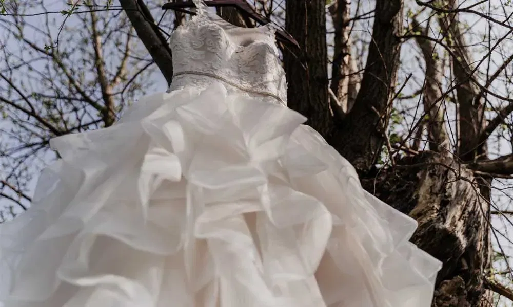 Romantisches Brautkleid mit Herzausschnitt und üppigem Tüllrock an einem Ast in natürlicher Umgebung aufgehängt