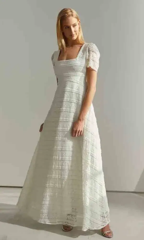 Weißes Hochzeitskleid mit hoch angesetzter Taille, gerafften Ärmeln und klarer Linienführung, getragen von einem Model mit offenen Haaren.