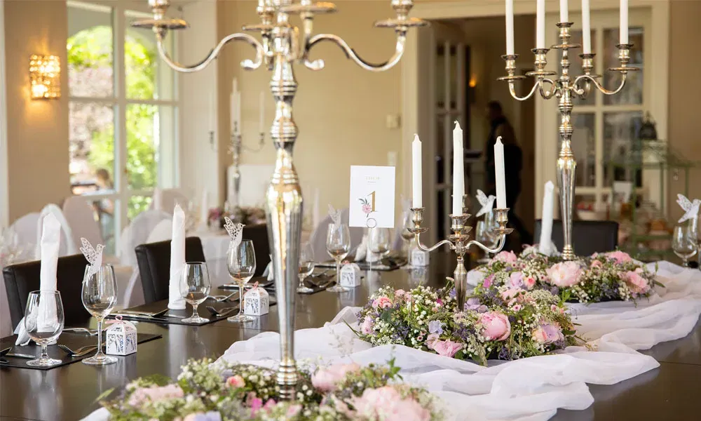 Festlich gedeckter Hochzeitstisch mit floralen Kränzen, weißen Servietten, Gläsern und silbernen Kerzenleuchtern.