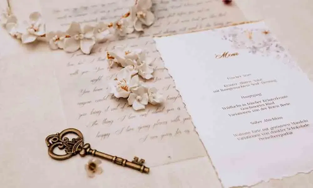 Romantisches Flatlay mit Menükarte, filigranen Blüten, einem antiken Schlüssel und kalligrafiertem Brief im Hintergrund.