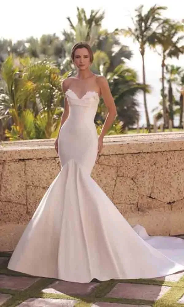 Strapless-Brautkleid in klarer Silhouette mit ausgestelltem Rock, fotografiert vor mediterranem Hintergrund mit Naturstein.