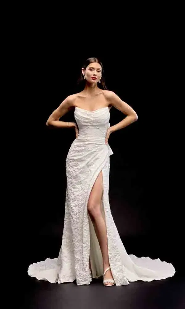 Extravagante Braut in trägerloser Robe mit strukturiertem Stoff und hohem Schlitz, dramatisch inszeniert im Studio.