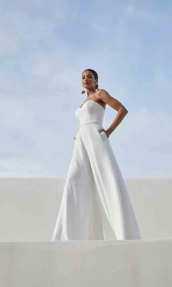 Stylische Braut in schulterfreiem Hosenanzug mit weitem Bein, aufgenommen im Freien vor klarem Himmel.