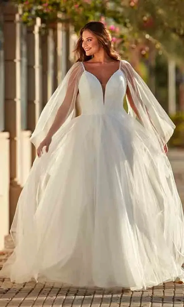 Strahlende Frau in märchenhaftem Hochzeitskleid mit Herzausschnitt und langen, durchscheinenden Flügelärmeln.