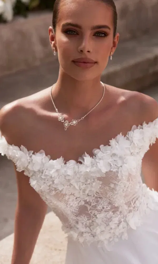 Detailreiche Ansicht eines Spitzenkleids mit floraler Schulterpartie – Braut mit dezentem Make-up in Tageslichtaufnahme.