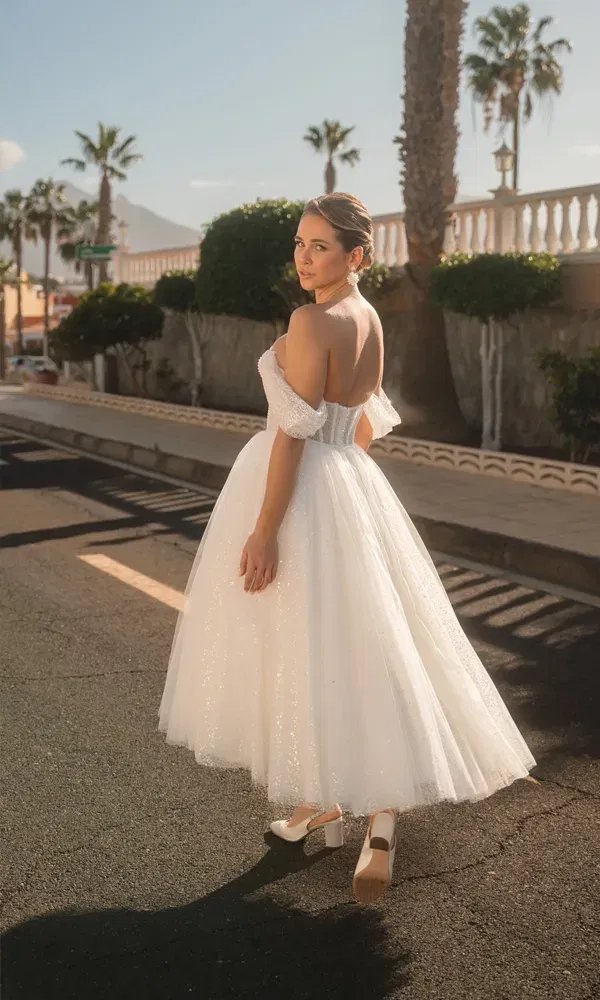 Zarte Brautszene: Eine Frau in weißem Korsettkleid mit weitem Rock schaut zurück in die Kamera, eingerahmt von Palmen und Straßenromantik.