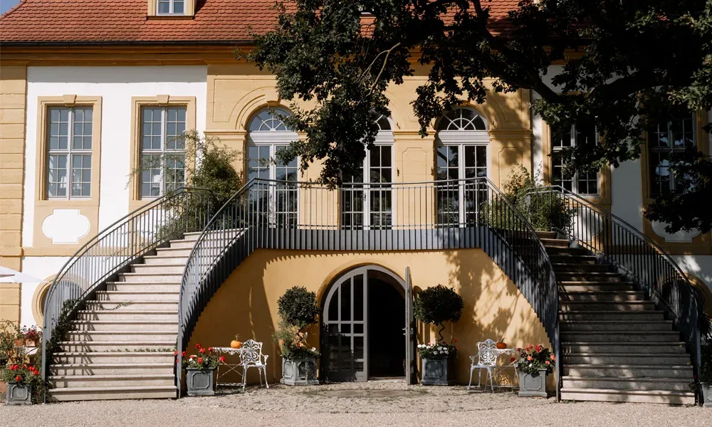 Zweistöckige Villa mit geschwungener Steintreppe, heller Putzfassade und Blumenarrangements am Eingang.