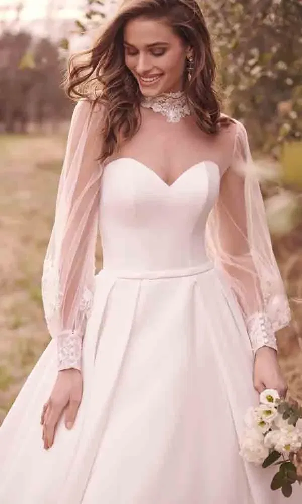 Schlichte Braut im A-Linien-Kleid mit transparenten Ärmeln, florale Spitze und Naturkulisse.