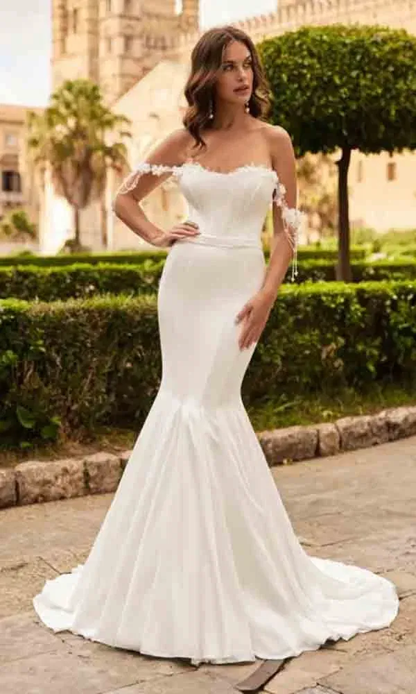 Off-Shoulder-Hochzeitskleid mit leicht ausgestelltem Rock und floralen Akzenten – stimmungsvoll inszeniert vor Schlossgarten-Atmosphäre.