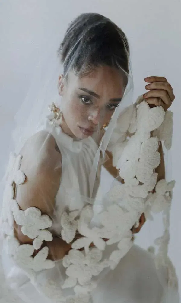 Braut blickt durch einen Schleier mit auffälligen Blütenverzierungen in sanfter, emotionaler Pose