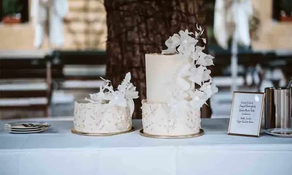 Kunstvolle Doppeltorte zur Hochzeit mit floralem Design und Acrylschild zur Geschmacksbeschreibung neben dem Arrangement.