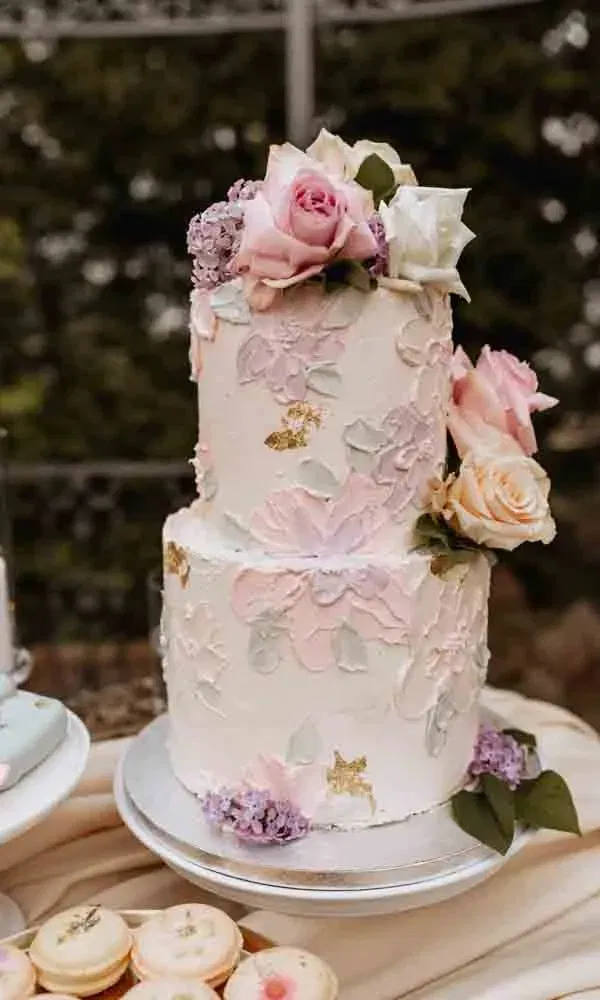 Bridgerton-inspirierte Hochzeitstorte mit Blütenmustern, frischen Blumen und pastellfarbener Deko auf Silberplatte.