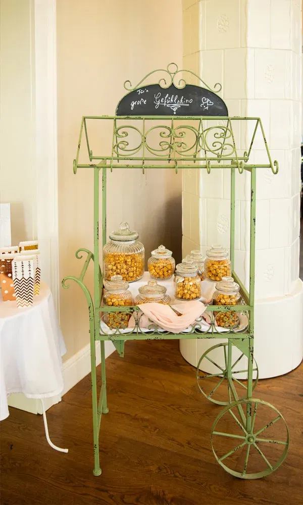 Detailreich gestalteter Popcornwagen mit Glasbehältern, einer rosa Serviette und Schild „Fürs große Gefühlskino“.