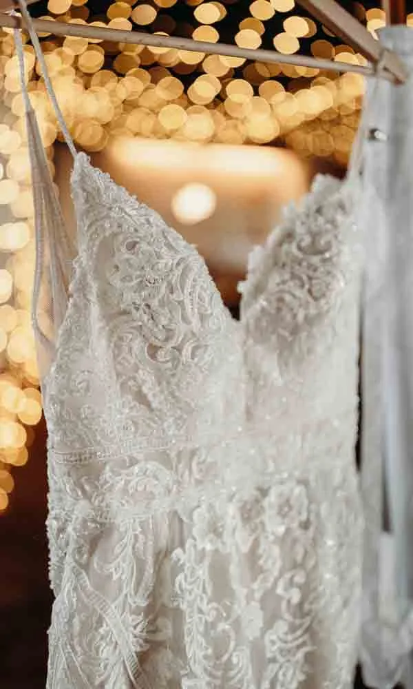 Zartes Brautkleid im Vintage-Stil hängt vor leuchtender Festbeleuchtung – bereit für den großen Tag.