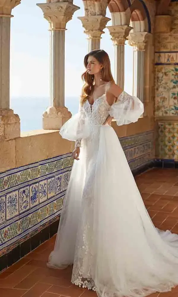 Elegant verspieltes Hochzeitskleid mit Tüllrock, zarter Spitze und auffälligen Organzaärmeln in traumhafter Outdoor-Kulisse.