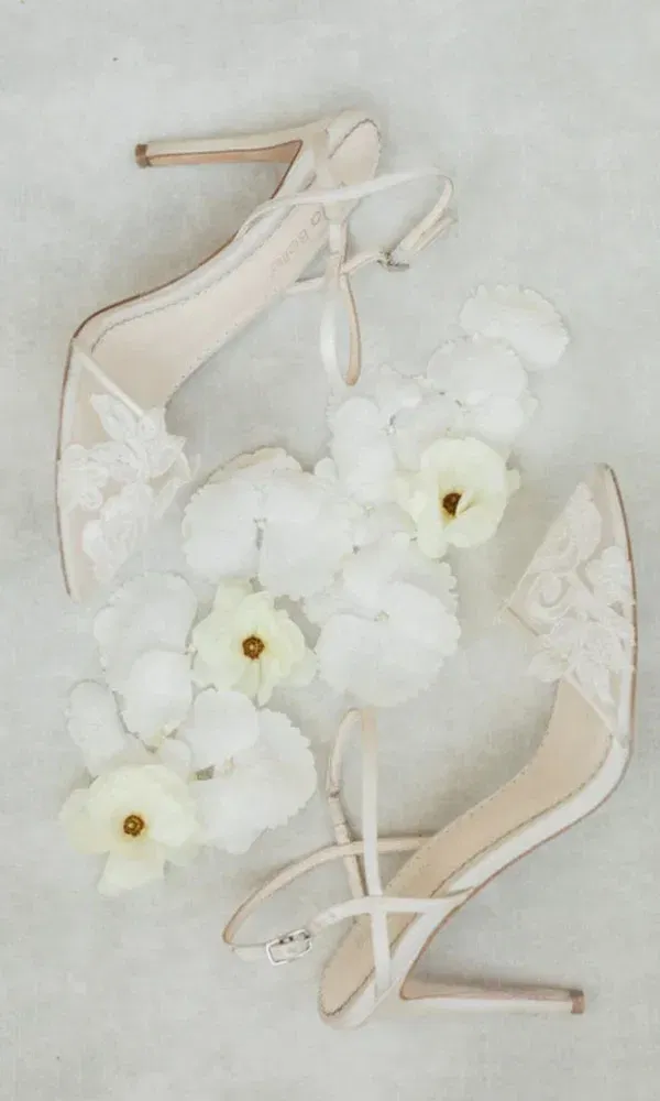 Verspielte High Heels mit floraler Verzierung, umgeben von weißen und cremefarbenen Deko-Blumen.