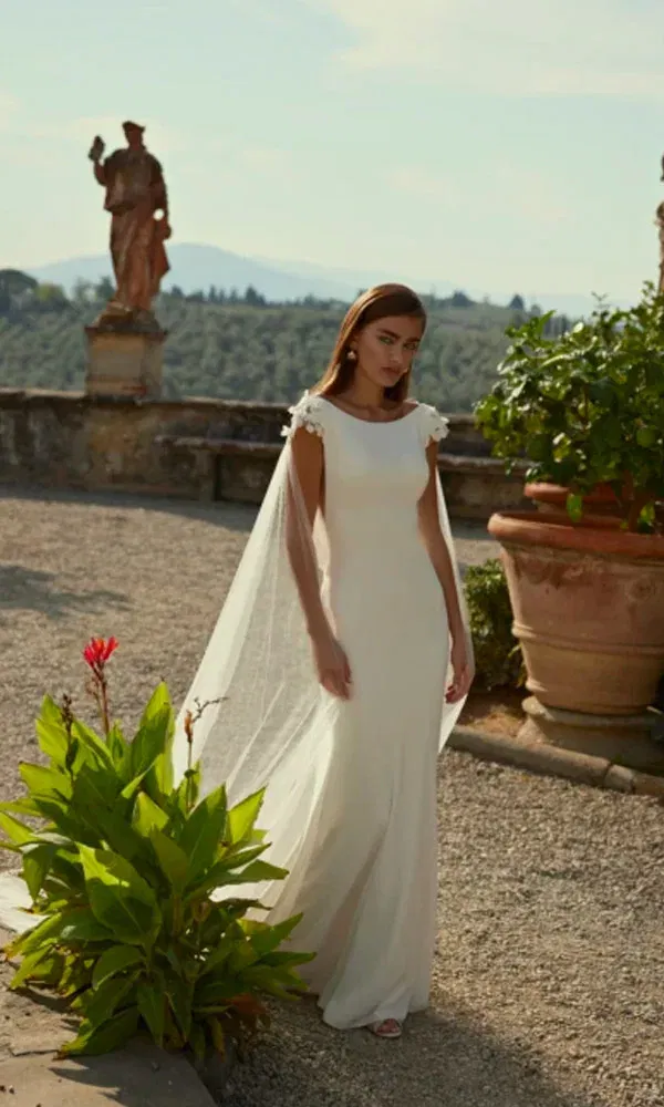 Stilvolle Szene mit Braut im weißen Kleid und durchscheinenden Capeschleiern zwischen Töpfen, Blumen und Naturstein.