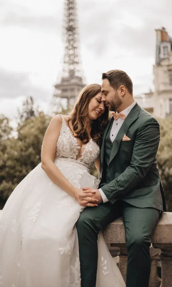 Katharina und Sebastian genießen einen vertrauten Moment in Hochzeitskleidung mit Blick auf den Eiffelturm.