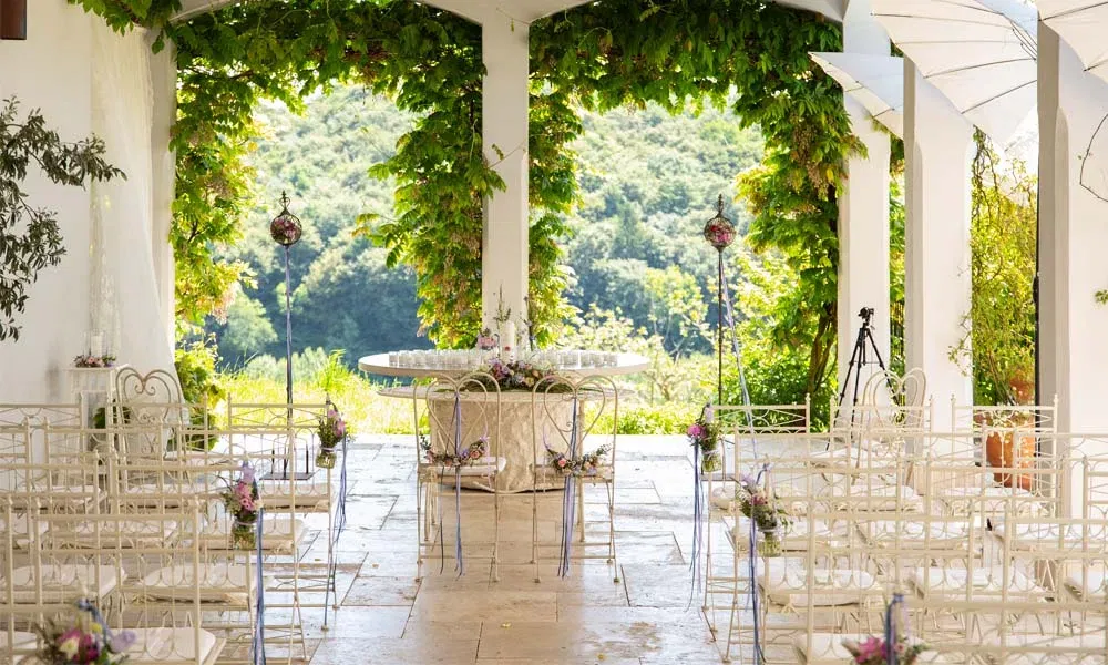 Romantische Outdoor-Traulocation mit weißen Stühlen, Blumenschmuck und Blick auf grüne Weinberge.