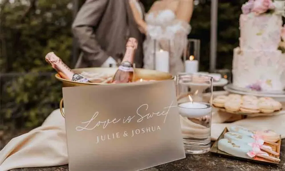 Romantisches Setting mit Champagner, Hochzeitskuchen, Gebäck und Namensschild von Julie & Joshua vor verschwommenem Brautpaar.