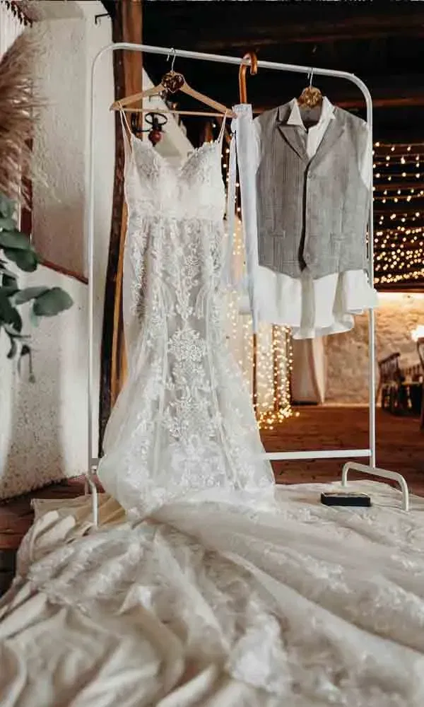 Zarte Spitze trifft auf Leinenstoff – das Hochzeitskleid und der Bräutigam-Look hängen bereit für den großen Tag in rustikalem Ambiente.
