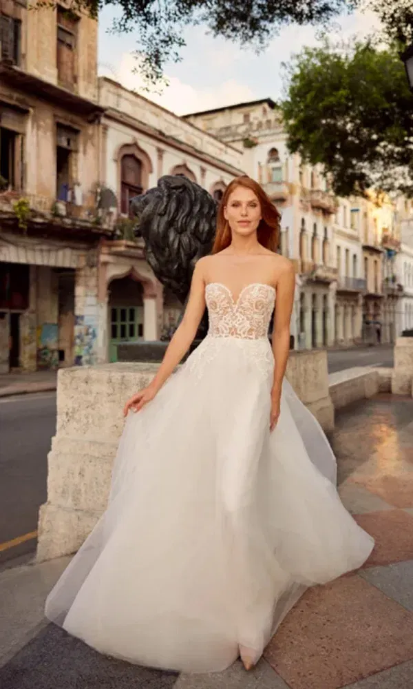 Rotes Haar und ein sinnliches Brautkleid: Eine Braut im modernen Spitzenlook steht selbstbewusst auf dem Gehweg einer Altstadt.