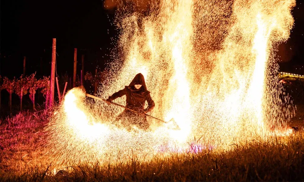Feuershow-Artist wirbelt brennenden Stab über dem Boden, Flammen und Funken sprühen spektakulär in die Höhe.