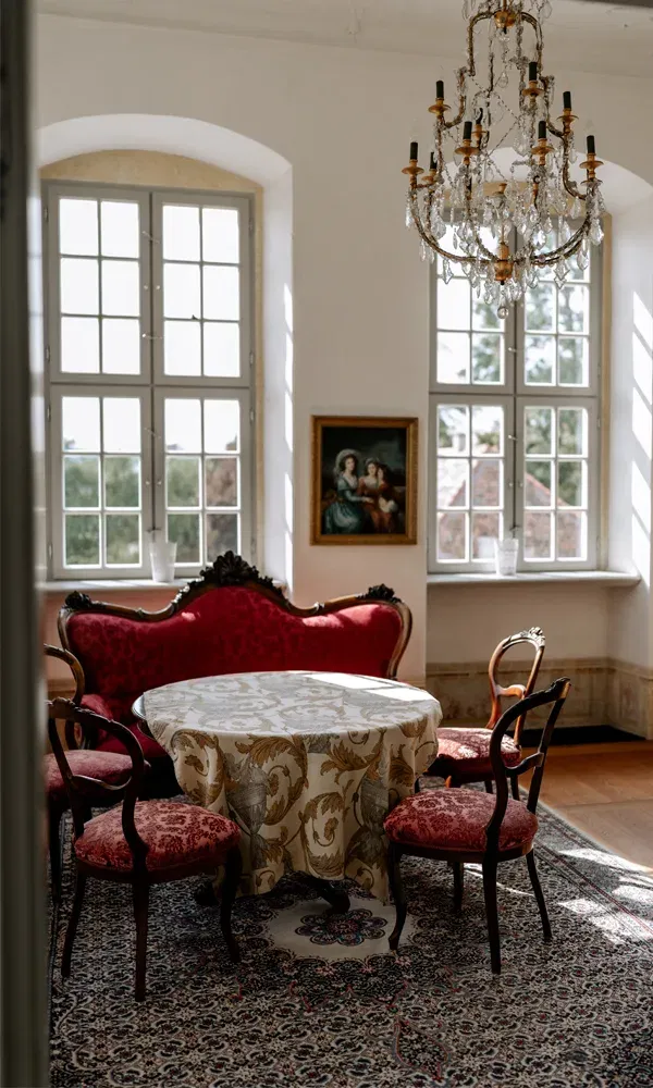 Heller Innenraum mit Teppich, verziertem Tisch, barockem Sofa und Kristalllüster – perfekte Kulisse für intime Gespräche.