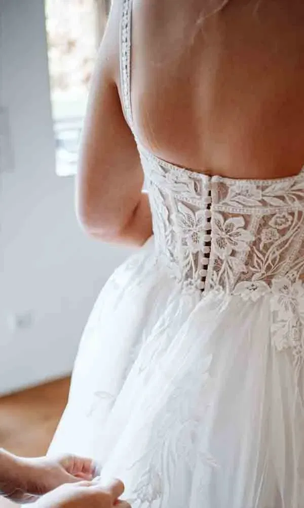 Brautkleid mit feinen Spitzenapplikationen und eleganter Knopfleiste – letzte Vorbereitungen am Hochzeitsmorgen.
