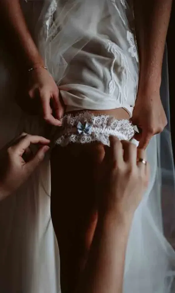 Detailaufnahme des Anziehens eines Spitzen-Strumpfbandes mit „Something Blue“-Element – festgehalten vor dem Jawort.