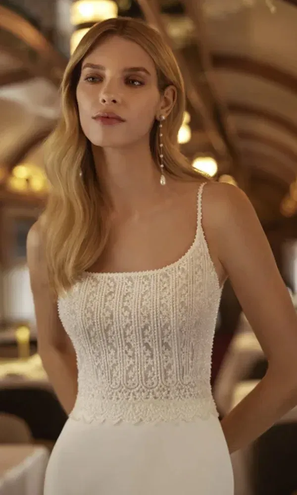 Detailreich verziertes Hochzeitskleid mit zarten Trägern und geometrischem Spitzenmuster, getragen von einer Braut im romantischen Ambiente eines Speisewagens.