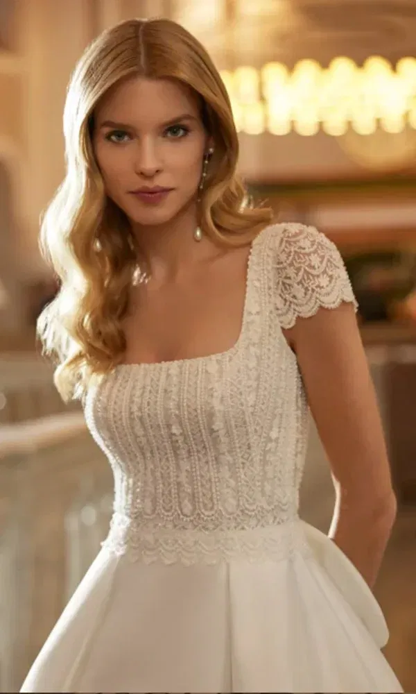Romantisches Brautoutfit mit strukturierter Spitze und klassischem Schnitt, getragen in stilvoller Indoor-Kulisse.