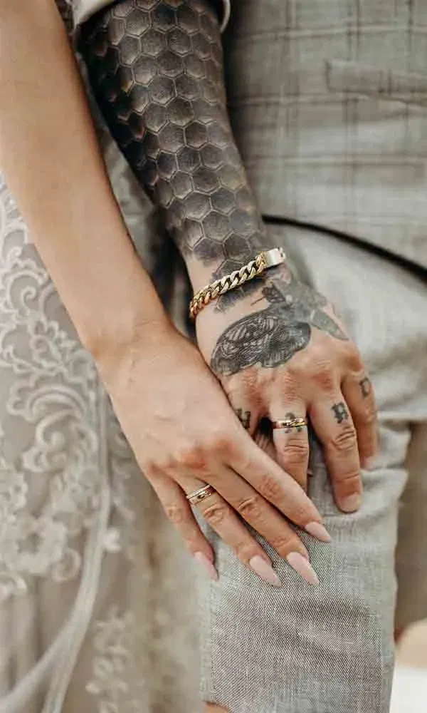 Hochzeitssymbolik im Close-up – Eheringe an tätowierten Händen, Brautspitze und Leinenstoff im natürlichen Boho-Stil.