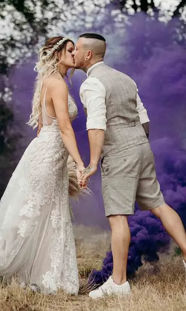 Kreativer Hochzeitsshot mit Farbeffekt: Braut und Bräutigam vor lila Smoke – ein Kussmoment voller Energie und Stil.