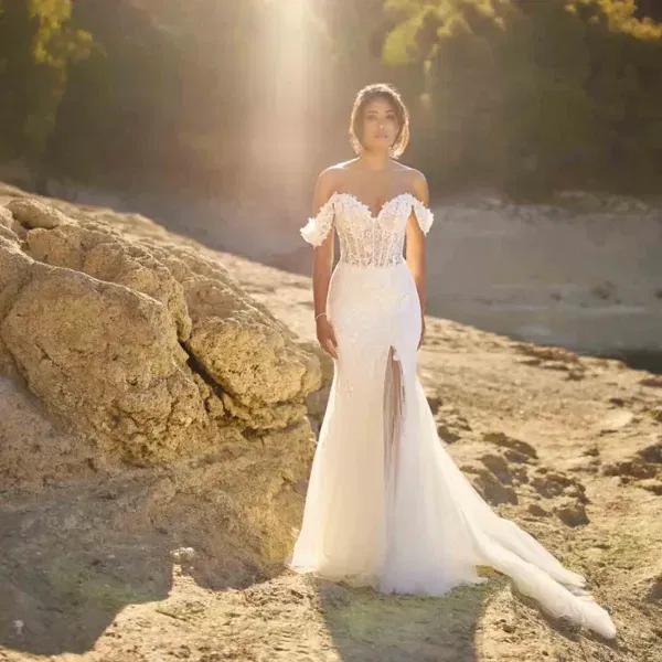 Eine Frau trägt ein modernes Brautkleid mit Herzausschnitt und transparentem Beinschlitz, fotografiert auf einer sonnenbeschienenen Felsenlandschaft.