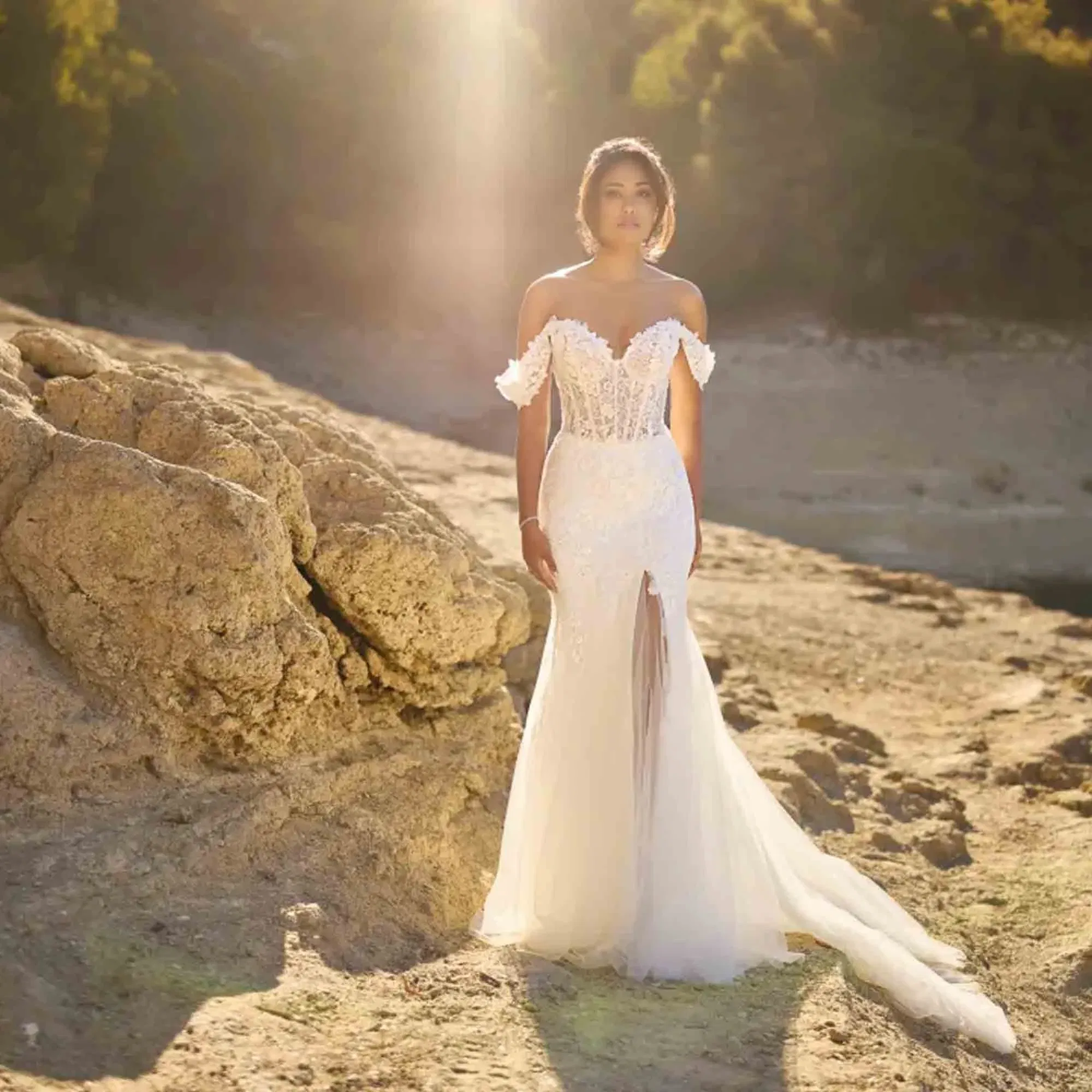 Eine Frau trägt ein modernes Brautkleid mit Herzausschnitt und transparentem Beinschlitz, fotografiert auf einer sonnenbeschienenen Felsenlandschaft.