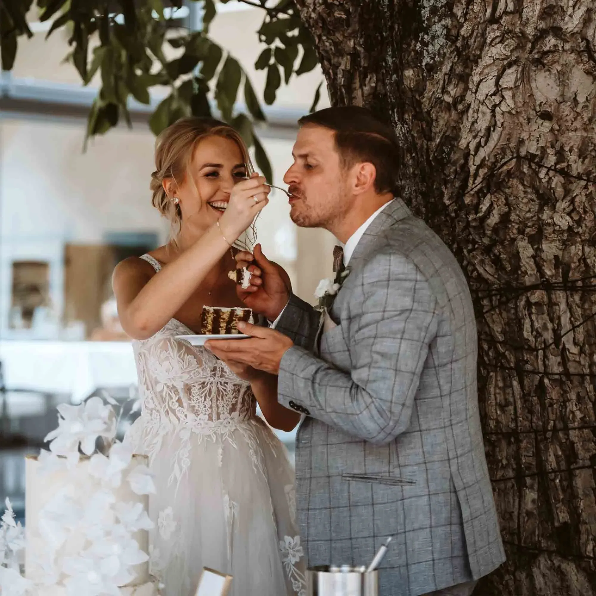 Brautpaar genießt gemeinsam ein Stück Hochzeitstorte in liebevoller Geste, umrahmt von Natur und Hochzeitsdeko.