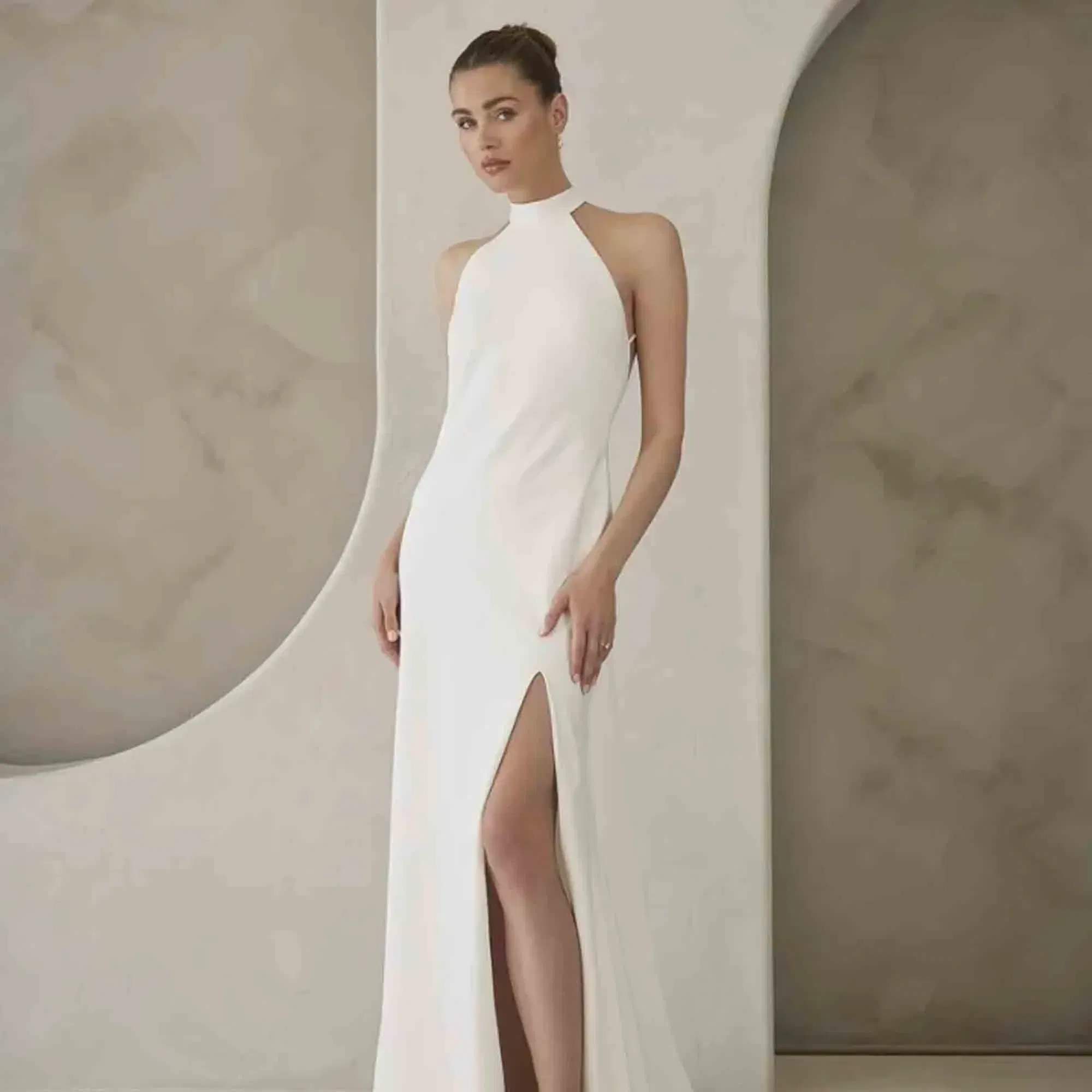 Modernes, körpernahes Hochzeitskleid mit Stehkragen und Beinschlitz, inszeniert in einem cleanen, geometrischen Setting.