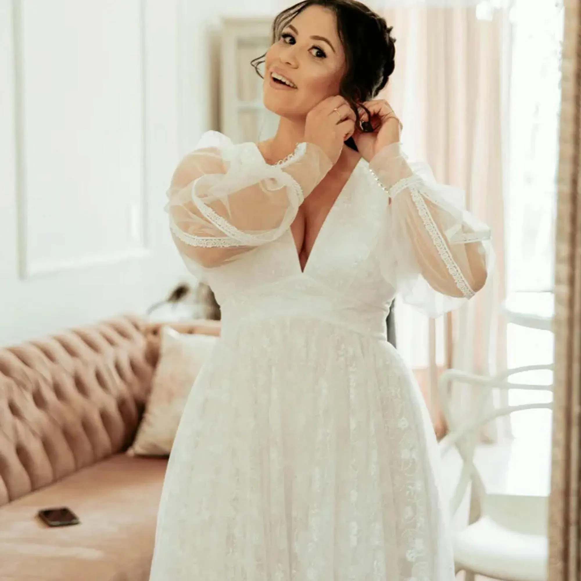 Frau in einem femininen Brautkleid mit Spitzenärmeln und betonter Taille bereitet sich im Ankleidezimmer auf ihre Hochzeit vor.