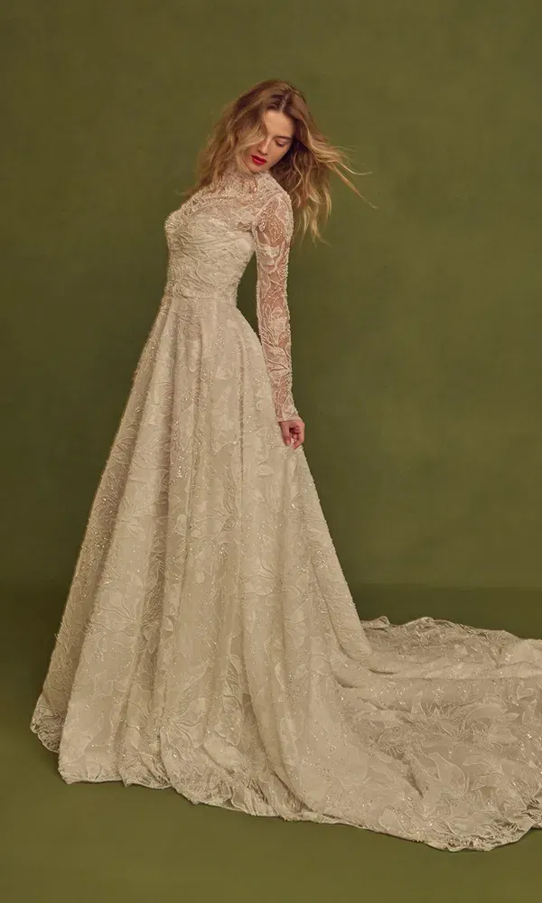 Romantisches Spitzenkleid mit langer Schleppe und strukturierter Silhouette, getragen von einer Braut mit offenem Haar, vor schlichtem, grünem Fotostudio-Setting.