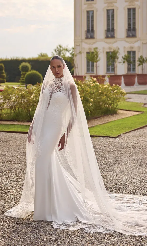 Eng anliegendes Kleid mit hohem Stehkragen und Spitzendetails unter langem, fließenden Schleier.