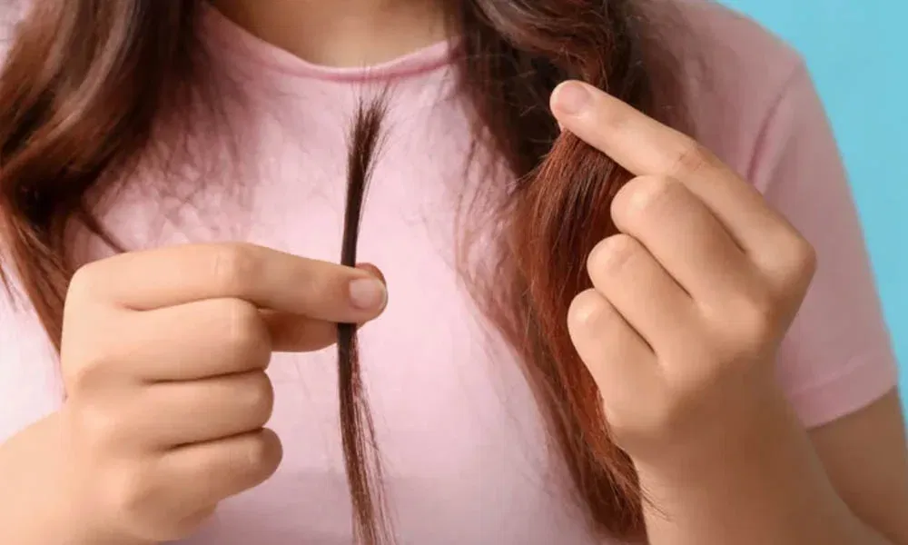 Frau hält eine einzelne Haarsträhne in den Händen vor einem blauen Hintergrund.