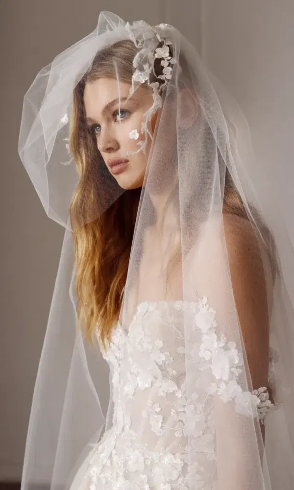 Zarter Hochzeitslook mit floralen 3D-Details und transparenter Lage – modernes Design trifft auf Klassik.