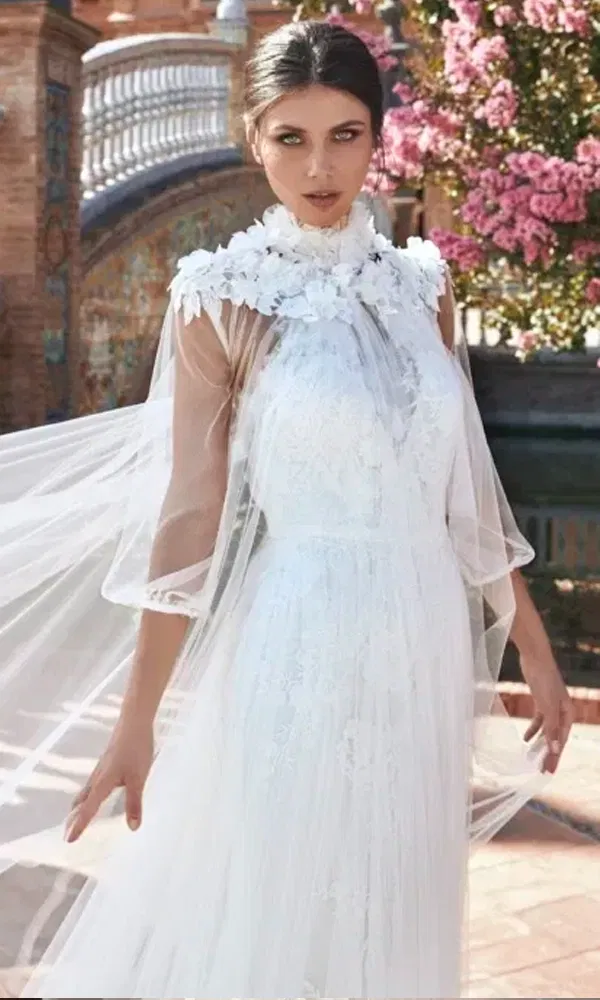 Extravagantes Brautkleid mit blütenbesetztem Cape und dramatischem Auftritt unter freiem Himmel.