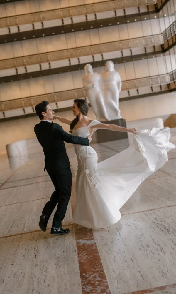 Brautpaar tanzt durch die Marmorhalle – Tiler in einem fließenden Kleid von Justin Alexander, Roman im klassischen Anzug.