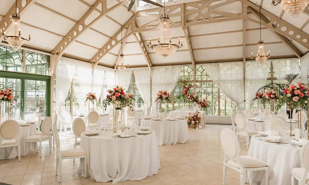 Elegant dekorierter Hochzeitssaal mit runden Tischen, weißen Stühlen und Blumenarrangements in kräftigen Pinktönen.