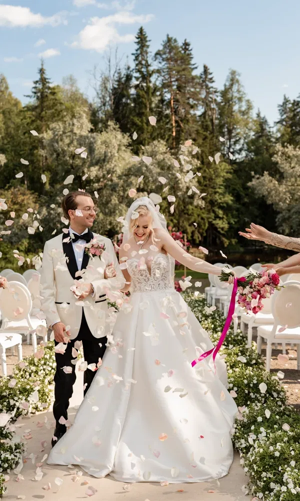 Braut und Bräutigam gehen lachend den Mittelgang entlang, umgeben von fliegenden Rosenblättern.