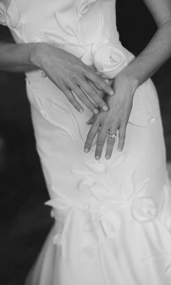 Eleganz im Detail: Tiler Pecks Hände ruhen sanft auf dem Kleid – der Ring glänzt im monochromen Bildausschnitt.