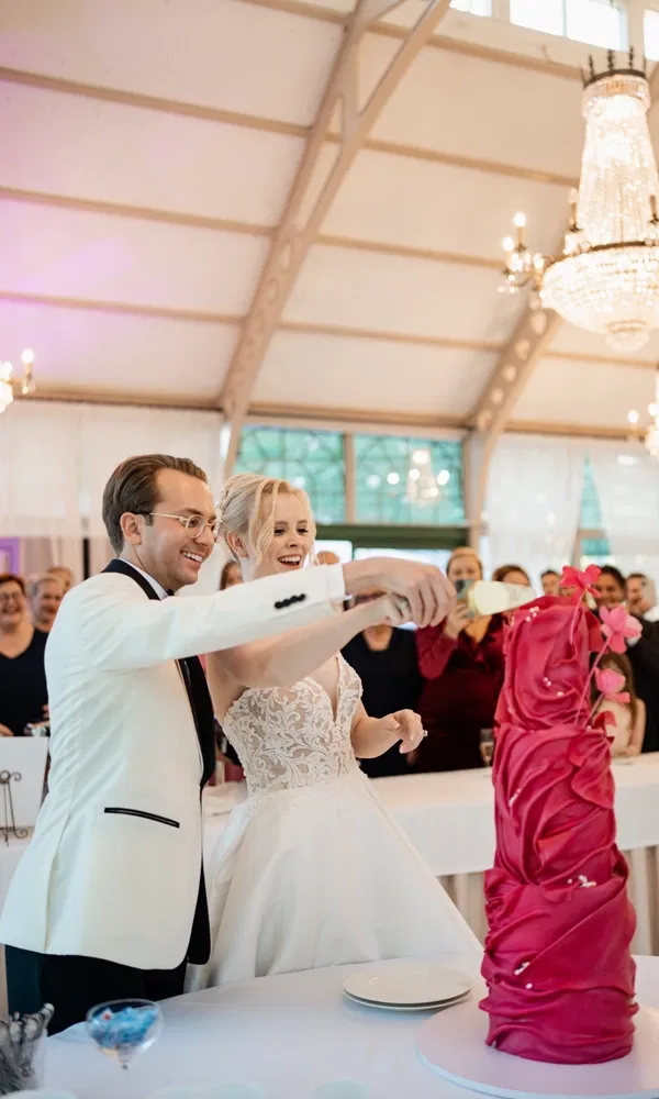 Braut und Bräutigam schneiden gemeinsam eine auffällige pinke Hochzeitstorte an.